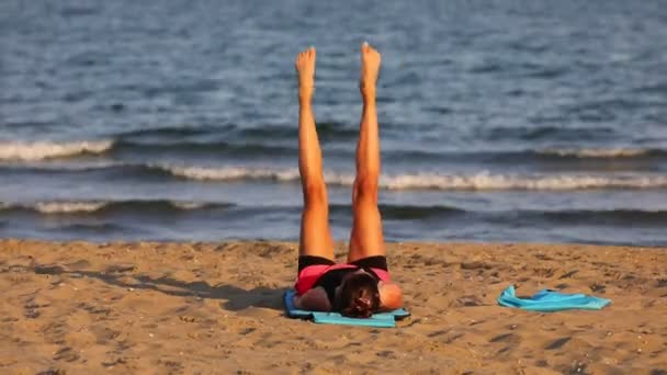 αθλητικό κορίτσι εκτελεί γυμναστικές ασκήσεις στην παραλία δίπλα στη θάλασσα - Πλάνα, βίντεο