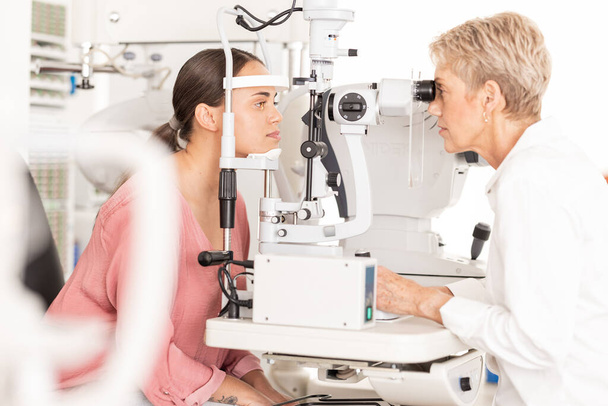Eyes, doctor and eye exam by woman consulting ophthalmologist for vision, eye care and sight at clinic. Optical, exam and eye health by women in a consultation room for optometry, check and diagnosis. - Photo, Image