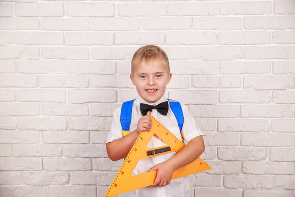Glücklicher Junge mit Down-Syndrom blickt durch das Loch eines großen Lineals in Form eines Dreiecks und macht sich bereit für die Schule. - Foto, Bild