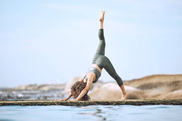 Yoga, stretching and black woman doing exercise at the beach, in yoga pose by water and rocks. Fitness, motivation and girl doing workout, training and exercising by sea for peace, wellness and calm. - Foto, Imagem