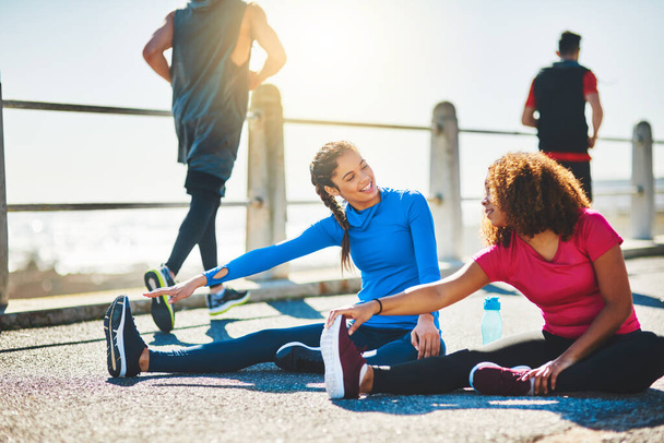 Workout buddies zijn een geweldige manier om motivatie te stimuleren. twee sportieve jonge vrouwen doen warming-up oefeningen samen buiten - Foto, afbeelding