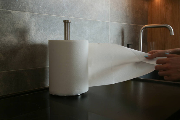 Žena v kuchyni tahá papírový ručník z rohlíku. Jednorázové savé papírové ručníky šetrné k životnímu prostředí pro použití v kuchyni, otírání povrchů nebo otírání rukou - Fotografie, Obrázek