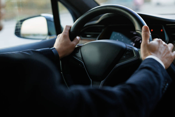 Male hands hold the steering wheel of a car, view from the inside of the cabin. Safety and attention on the road. Driving vehicles. Unrecognizable businessman putting his hands on steering wheel. - 写真・画像