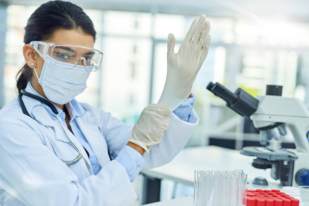 Давайте поэкспериментируем. Портрет молодого учёного, надевающего защитные перчатки во время работы в лаборатории - Фото, изображение