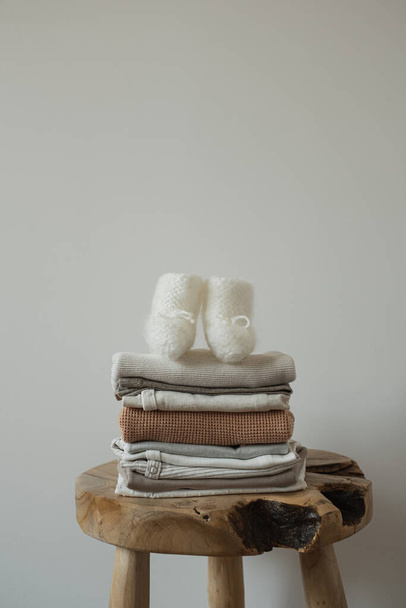 Stack elegáns, elegáns újszülött babaruha, zokni fa széklet közelében fehér fal. Semleges pasztell bézs szín - Fotó, kép