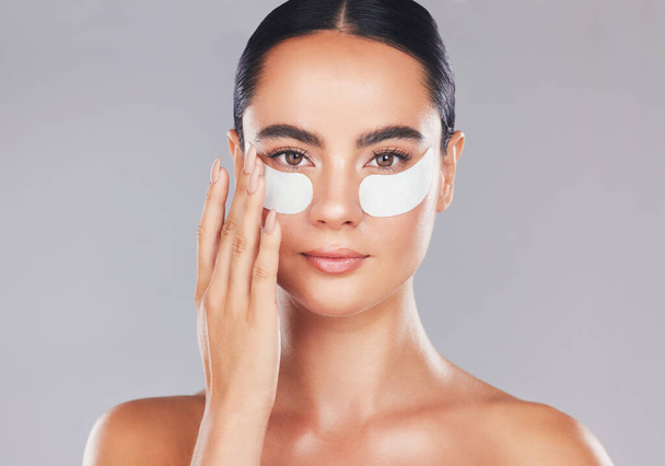 Skincare, face and woman with eye patches on a gray studio background. Health, beauty or female model from Spain with facial product, cosmetics pads or collagen eye mask for hydration or anti aging. - Photo, Image