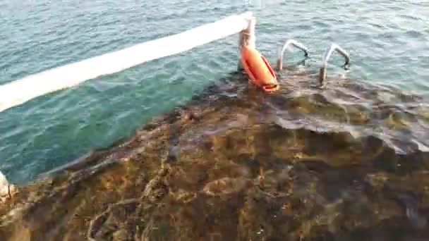 Oranje boei op de pier in de zee van dichtbij in geval van nood. Pier met ladder in de lichtblauwe zee - Video