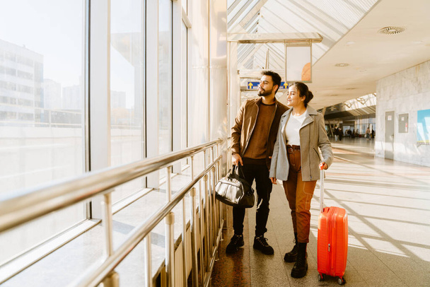 Young indian couple looking in window together at airport indoors - Photo, image