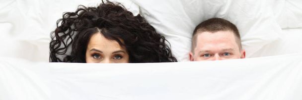 男性と女性の白い毛布で覆われ、悪い目を覚ますカップルの上のビュー。カベレー帽の下に隠れて愛のカップル。おはよう、家族と甘い家庭の概念 - 写真・画像