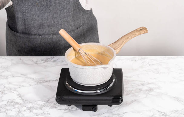 Приготовьте глазурь из ирисок в небольшой кастрюле с соусом над электрической плитой. - Фото, изображение