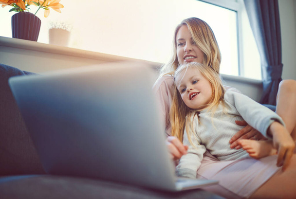 Családi időtöltés a technológia jóvoltából. egy aranyos kislány, aki laptopot használ az anyjával otthon a kanapén. - Fotó, kép