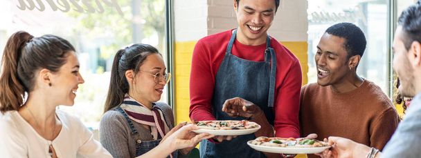 Horizontální banner nebo záhlaví s číšníkem servírující lahodné pizzy margherita pro multikulturní přátele v útulné pizzerie restaurace - Multiethnic přátelé baví společně v pizzerii - Fotografie, Obrázek