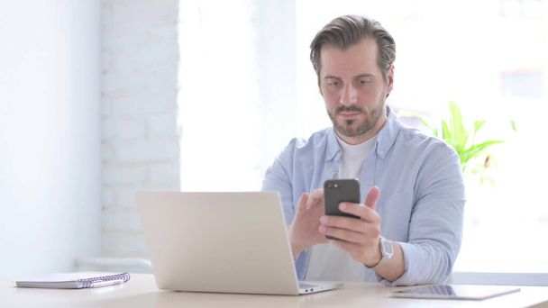 Mature Man using Smartphone while using Laptop - Zdjęcie, obraz