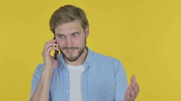 Casual Young Man Talking Angry on Phone on Yellow Background - Photo, image