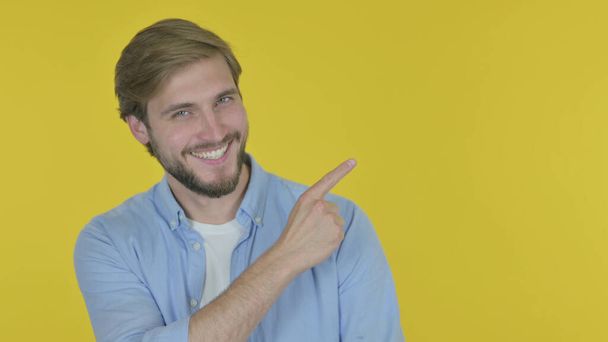 Casual Young Man Pointing on Side on Yellow Background - Photo, image