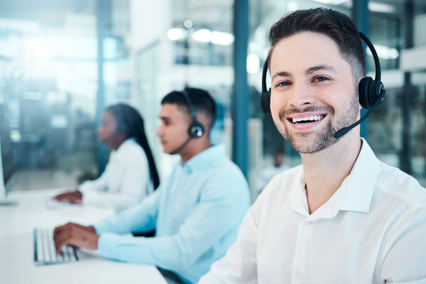 Call center, telemarketing, and customer service consultant wearing a headset and looking happy at the office. Contact us and crm agent man with sales team for support, help and service with a smile. - 写真・画像