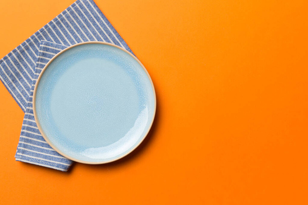 Bovenaanzicht op gekleurde achtergrond leeg ronde Blauwe plaat op tafelkleed voor voedsel. Lege schotel op servet met ruimte voor uw ontwerp. - Foto, afbeelding