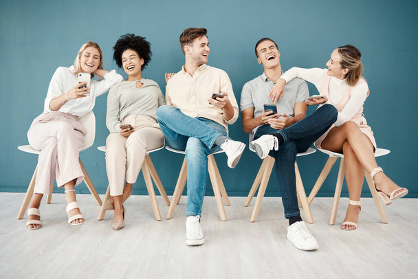 Hiring, phone and recruitment with people in a room waiting, laughing and bond before interview, relax and happy. Candidate, unemployed and group sharing funny online meme, joke or social media. - Photo, Image