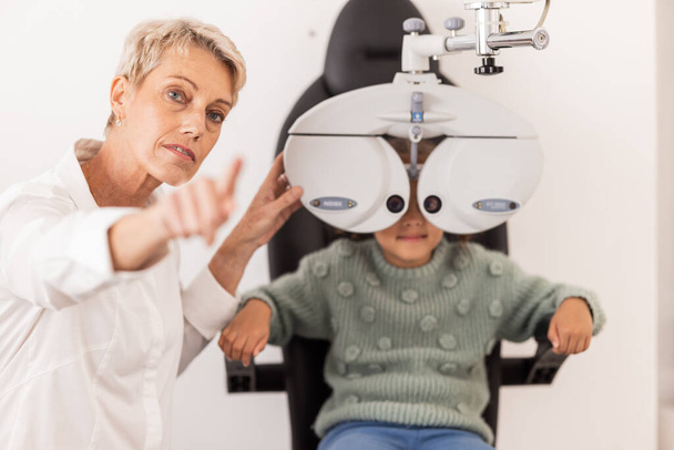 Visie, oog en test met een kind bij optometrie onderzoek met een specialist in een kliniek voor glazen. oogheelkunde, optometrie en medisch deskundige oogtest met klein meisje voor ooggezondheid en oogverzorging. - Foto, afbeelding
