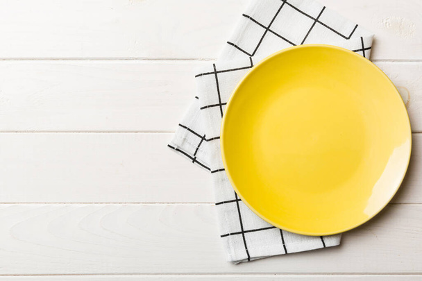 Vista superior sobre fondo de color vacío placa redonda amarilla en mantel para la comida. Plato vacío en servilleta con espacio para su diseño. - Foto, Imagen