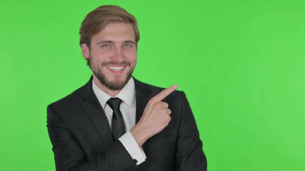 Young Adult Businessman Pointing on Side on Green Background - Foto, Imagen