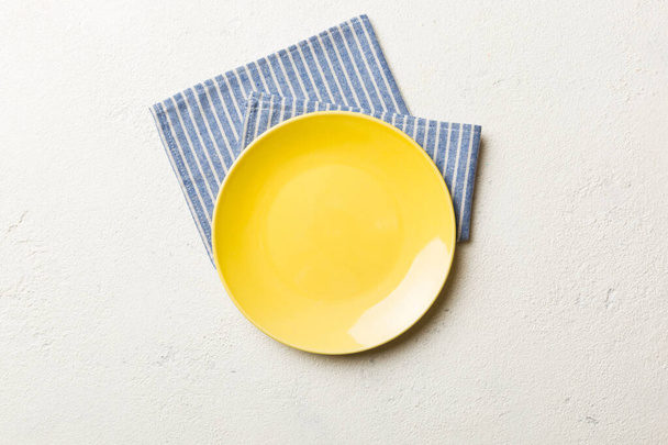 Top view on colored background empty round yellow plate on tablecloth for food. Empty dish on napkin with space for your design. - Photo, Image