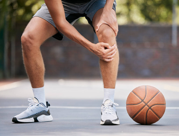 Pain, basketball and man with knee injury standing on outdoor court, holding leg. Sports, fitness and athlete with joint pain, injured and hurt in training, workout and game on basketball court. - Foto, Bild
