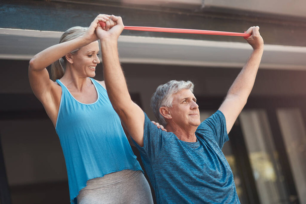 Keep your focus and pain will go away. a mature man stretching his arm muscles with an elastic band while being assisted by a woman - Photo, Image