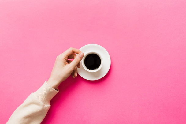 Minimalistic style woman hand holding a cup of coffee on Colored background. Flat lay, top view espresso cup. Empty place for text, copy space. Coffee addiction. Top view, flat lay. - Photo, Image