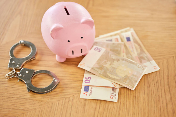 Piggy bank, money and handcuffs fraud crime for euro scam, corruption and criminal wealth exchange. Economy crisis, bankruptcy and illegal euros for taxes bribe or bank dollars payment offer - Foto, Imagem