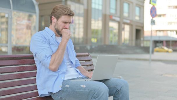 Tosse uomo di mezza età utilizzando il computer portatile mentre seduto all'aperto sul banco - Foto, immagini