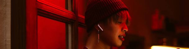 Asian boy listening music with earphones while standing in doorway - Фото, изображение