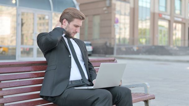 Middle Aged Businessman with Neck Pain Using Laptop while Sitting Outdoor on Bench - Photo, image