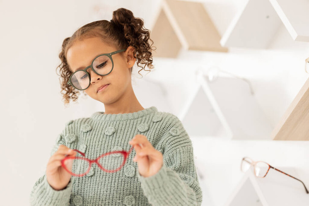 Glasses, options and children with a girl in an optometry store while shopping for prescription lenses. Kids, retail and vision with a female child customer looking at eyewear at the optometrist. - Foto, Bild