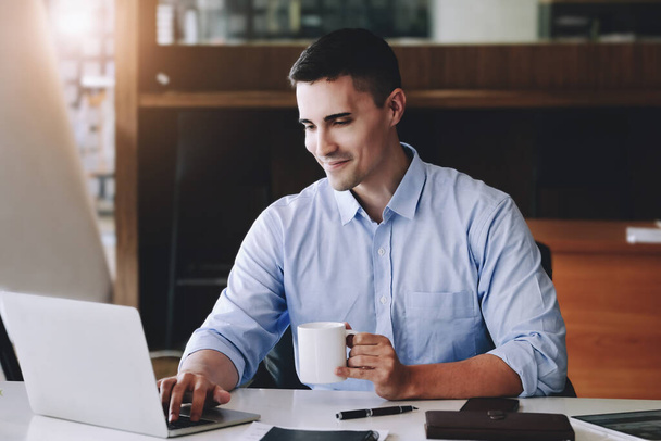 Männliche Marketingmanager trinken Kaffee, während sie arbeiten, um Schläfrigkeit zu reduzieren, bevor sie Computer, iPads und Marketinganalysen verwenden - Foto, Bild