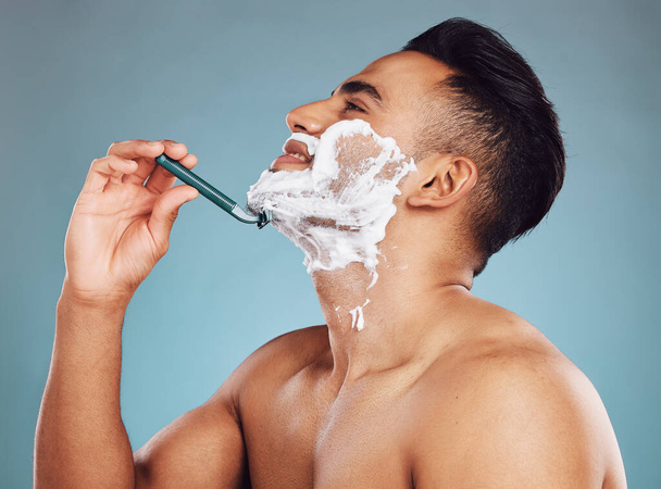 Στούντιο, περιποίηση δέρματος και άντρας να ξυρίζει τα γένια του σε μια καθημερινή πρωινή ρουτίνα καλλωπισμού με ξυράφι στο Μεξικό. Χαμόγελο, ευεξία και χαρούμενος Λατίνος ξυρίζει το μουστάκι ή τα μαλλιά του προσώπου του για την υγιεινή της προσωπικής του φροντίδας. - Φωτογραφία, εικόνα