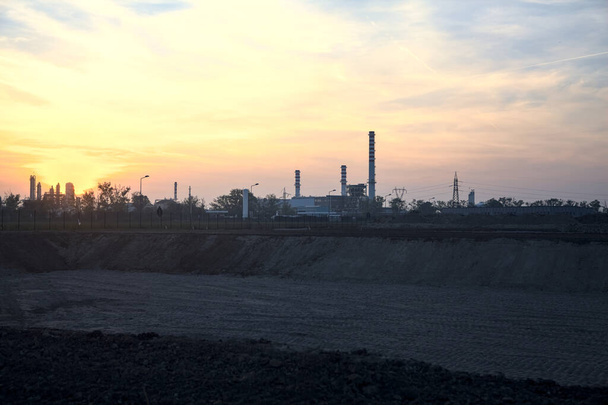 Промисловий комплекс на горизонті за межами голого поля на заході сонця
 - Фото, зображення