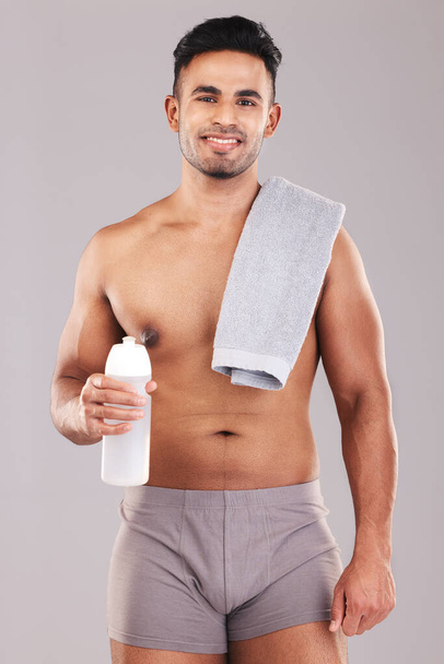 Man, body and water bottle for fitness on studio background in workout, training or exercise for health, wellness or strong muscles. Portrait, smile and happy sports athlete with drink or sauna towel. - Foto, Bild