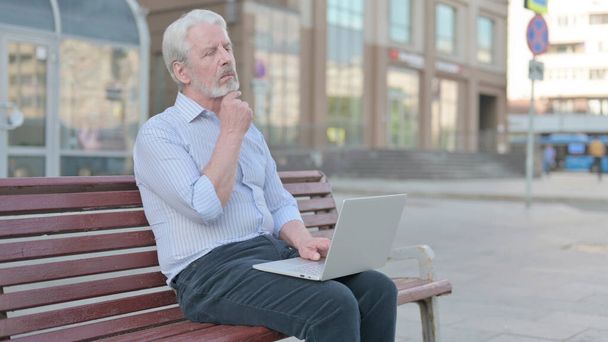 Thinking Senior Old Man Using Laptop while Sitting Outdoor on Bench - Foto, imagen