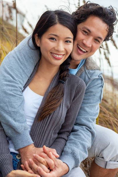 Joven asiático chino hombre y mujer, chico chica, pareja sentado en la hierba alta sonriendo con dientes perfectos en una cita romántica al aire libre - Foto, imagen