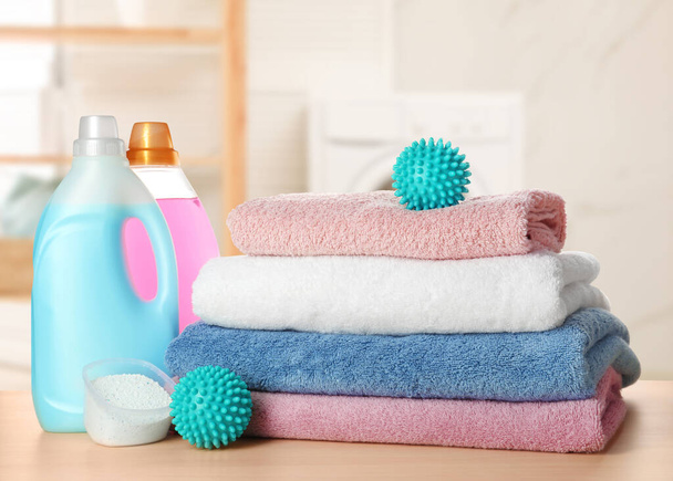 Dryer balls, detergents and stacked clean towels on wooden table in laundry room - Photo, image