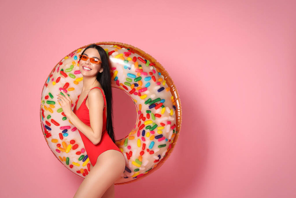 Young woman with stylish sunglasses holding inflatable ring against pink background - Photo, image