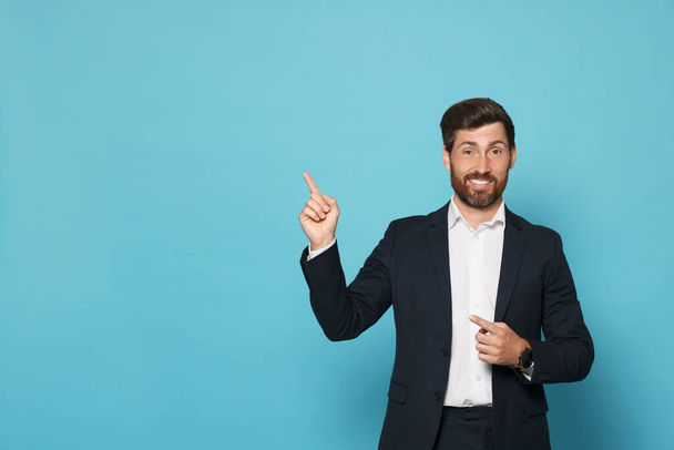 Smiling bearded man pointing index finger up on light blue background. Space for text - Foto, immagini