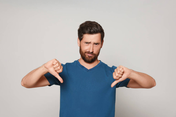 Handsome bearded man showing thumbs down on light grey background - Foto, Imagem