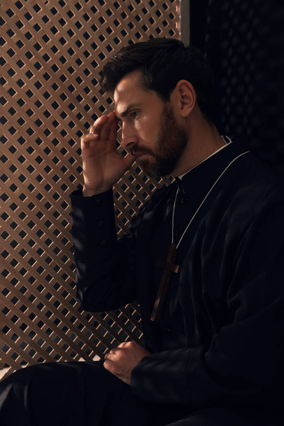 Catholic priest wearing cassock in confessional booth - Valokuva, kuva