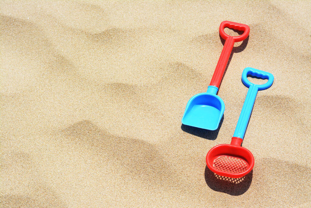 Plastic shovel and sieve on sand, space for text. Beach toys - Fotó, kép