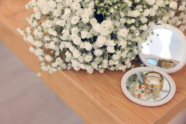 Pocket mirror, engagement rings and beautiful bouquet on wooden table. Wedding day - Fotoğraf, Görsel