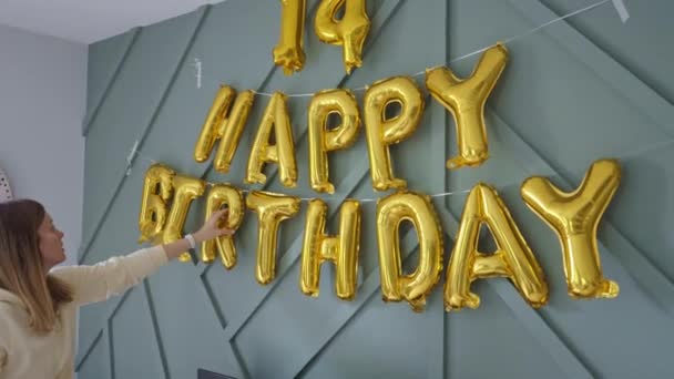 Moeder versiert woonkamer met ballonnen voor het vieren van de verjaardag van het kind. Thuisfeest voor zoon. Inschrijving gefeliciteerd met je verjaardag op de muur - Video