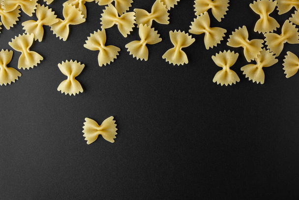 Raw pasta farfalle with copy space on black background. Top view of Italian cuisine ingredient. - Foto, imagen