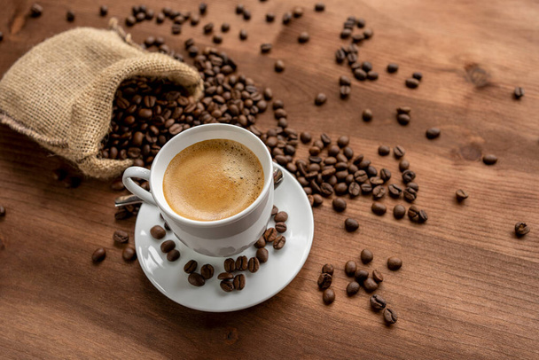 Tasse heißen Kaffee auf rustikalem Holztisch und ein Sack voller Kaffeebohnen. - Foto, Bild